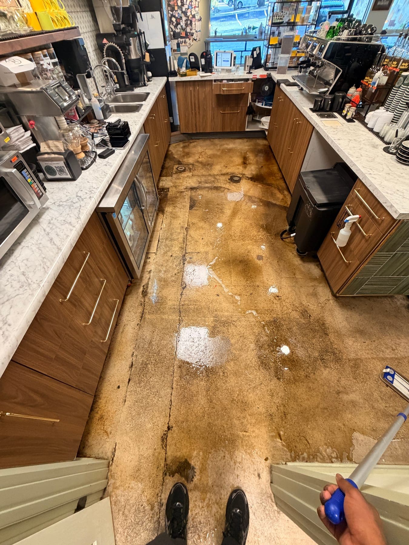 Heavily soiled café concrete floor being degreased and scrubbed, with cleaned sections showing through
