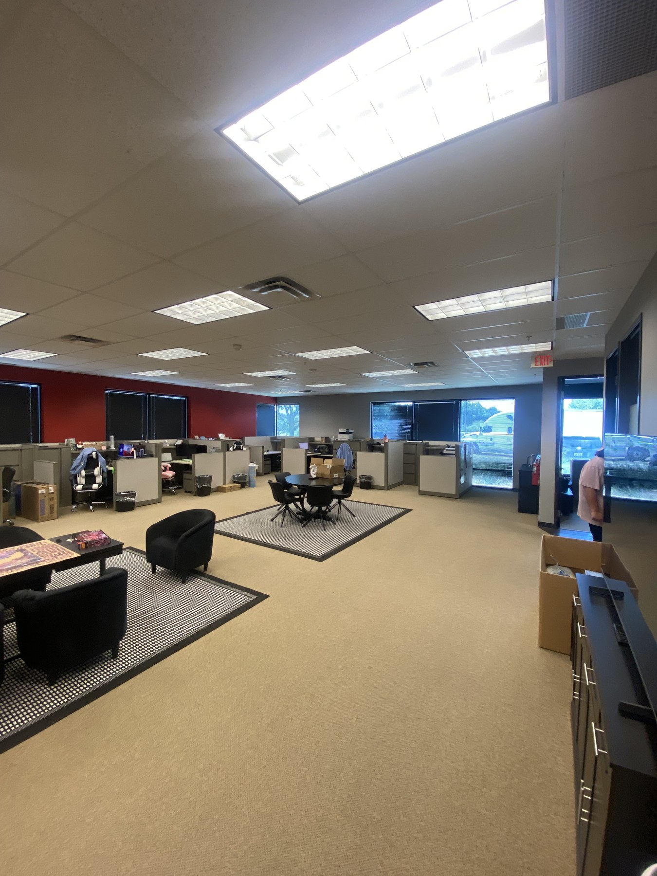 Open-plan office with grey cubicle pods, beige broadloom carpet, a dark red accent wall and lounge chairs on area rugs