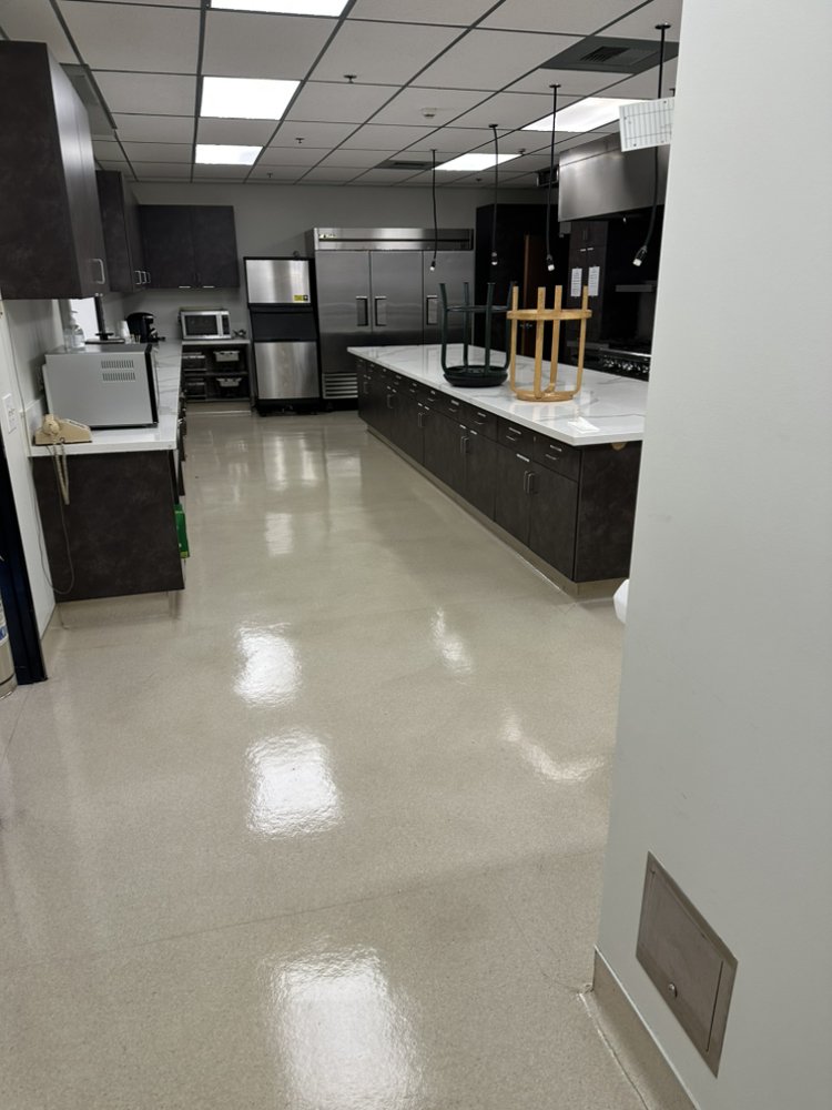 Break-room kitchen with dark cabinets and white counters over vinyl composition tile stripped and waxed to a gloss